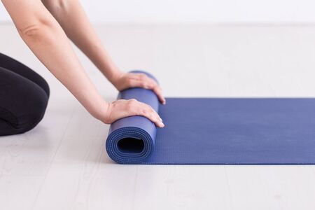 Young girl in training outfit rolling up the blue mat. Selective focus.の写真素材