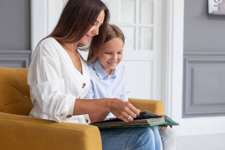 Daughter, mother and grandmother sit in chair with photo album in handsの写真素材