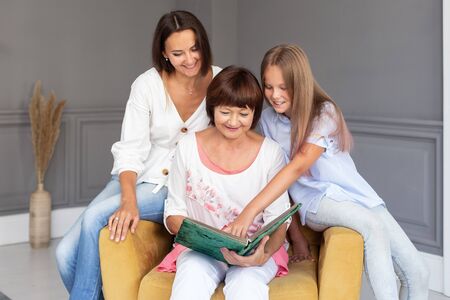 Little girl points at album while sits with her mother and grandmotherの写真素材