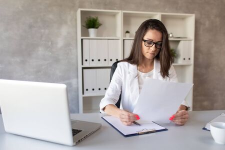 The dark-haired businesswoman looks in surprise at what is written on a piece of paper in her hands. Selective focusの写真素材