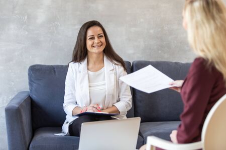 Cute woman smiles to woman with sheet of paper in hands in front of her. Selective focusの写真素材