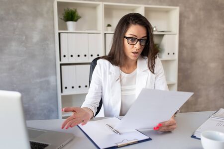 The dark-haired businesswoman looks in surprise at what is written on a piece of paper in her hands. Selective focusの写真素材