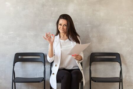 Black-haired women holds sheet of paper in one hand and shows OK gestureの写真素材