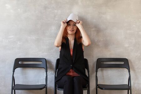 Redhead woman holds her resume bove her head sitting on chair in officeの写真素材