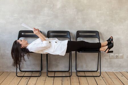 Woman in casual clothing lays on chairs and reading text from sheet of paperの写真素材