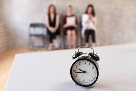 Closeup of mechanical clocks on table in office. Three women sits in chair on background. Selective focusの写真素材
