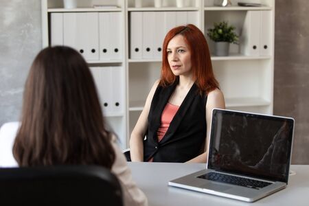 Cute redhead woman sits behind office table at job interview. Selective focusの写真素材