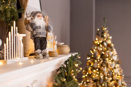Toy Santa Claus stands on white fireplace and decorated Christmas tree stnads on background. Selective focusの写真素材