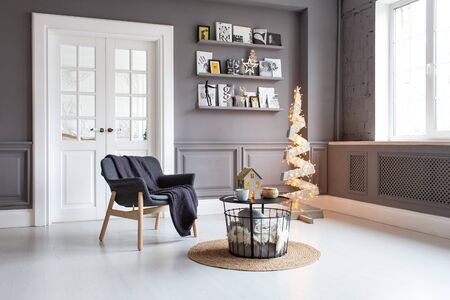 Nizhniy Novgorod, Russia - November 11, 2019: Photo studio 2.8. Living room with chair, table, shelf and wooden tree decorated with garlandのeditorial素材