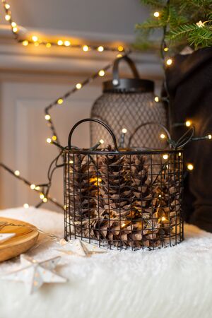 Closeup of basket full of fir cones on background of wall covered in shining garland. Selective focusの写真素材