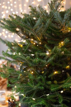 Christmas tree covered in lights on background of shiny garland on gray wallの写真素材
