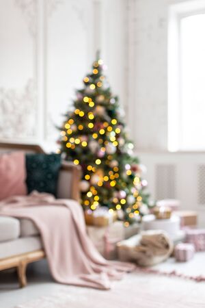 Blured photo of decorated wit garland and toys christmas tree standing next to white sofa.の写真素材
