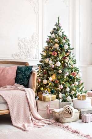 Christmas tree decorated by garland and gift boxes stands close to sofaの写真素材