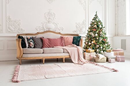 Christmas tree surrounded by giftboxes stands close to sofa in living roomの写真素材