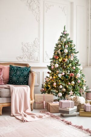 Lots of gif boxes lay next to sofa and decorated with garland and toys christmas tree. Selective focusの写真素材