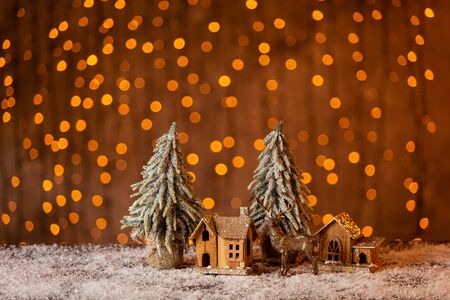 Two decorative fir trees stand next to tiny wooden houses and toy elk. Selective focusの写真素材