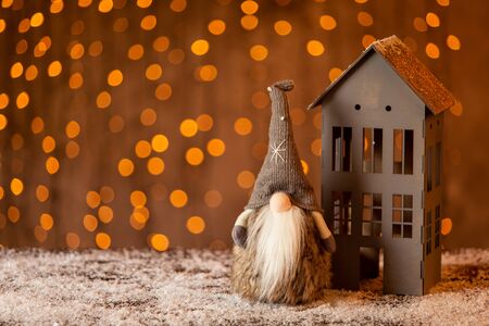 Little figure of gnome stands next to gray house made of paper. Selective focusの写真素材
