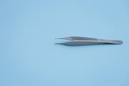 Steel dental tweezers on light blue background