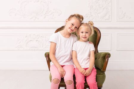 Two little blond sit in green armchair and hug each otherの写真素材