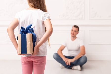Blond little girl hides giftbox behind her back and prepare to give it to her father. Selective focusの写真素材