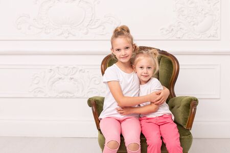 Two little blond sit in green armchair and hug each otherの写真素材