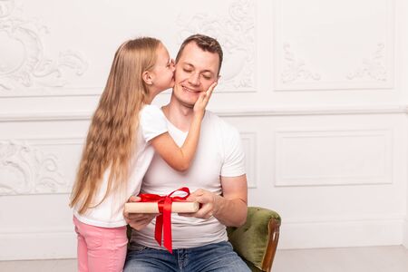 Little girl kiss her father, who hold giftbox in hand, in cheek. Selective focusの写真素材