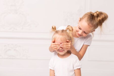 Older sister closes eyes of smiling younger one with palmsの写真素材