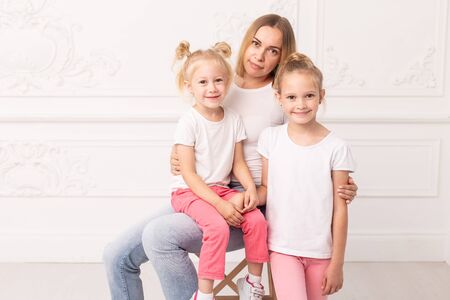 Mother who sits on chair and her daughters standing next to her pose for a photoの写真素材