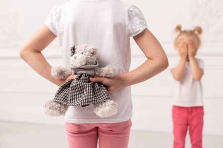 Little girl in pink pans hides toy bear preparing to make gift to her sister. Selective focusの写真素材