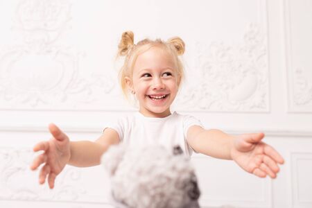 Little blond girl smiles and prepare to accept toy bear as gift. Selective focusの写真素材