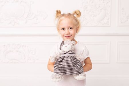 Little blond cheerful girl holds toy bear in hands and smileの写真素材
