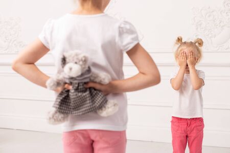 Little girl in pink pans hides toy bear preparing to make gift to her sister. Selective focusの写真素材