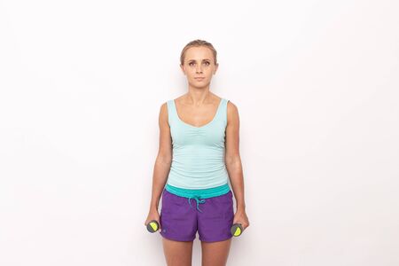 Lean woman in sport outfit with dumbells in hands on white isolated backgroundの写真素材