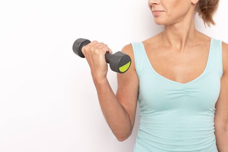 Closeup of dumbbell in hands of lean woman in blue top. Empty space for text. White isolated backgroundの写真素材