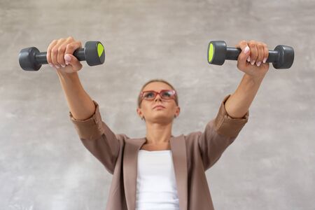 Cute woman in casual clothing holds two dumbbells in hands and looking forward. Selective focusの写真素材