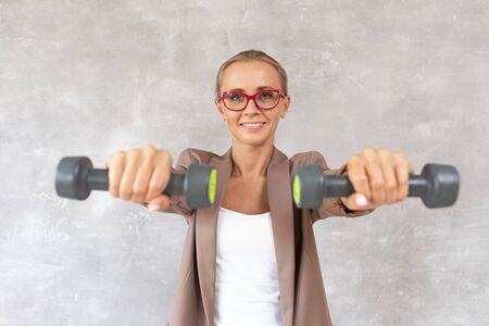Charming blond woman holds dumbbells in hands in front of herself. Selective focusの写真素材