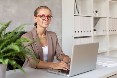 Smiling office worker sits in chair behind laptopの写真素材