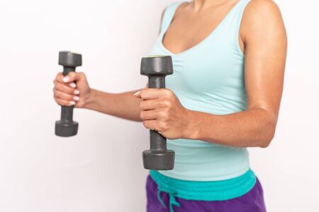 Two dumbbells in hands of woman in sport outfit. Selective focus. White isolated background.の写真素材