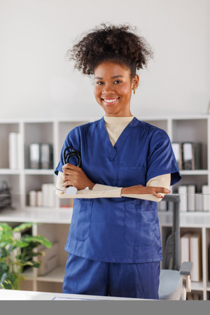 Medical professional in blue scrubs working on laptop, woman smiling while standing in well-lit...