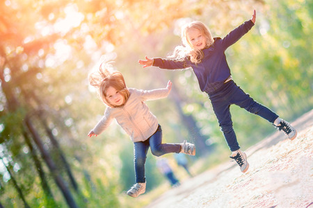 Two little girls jumping and having fun together outdoorsの写真素材
