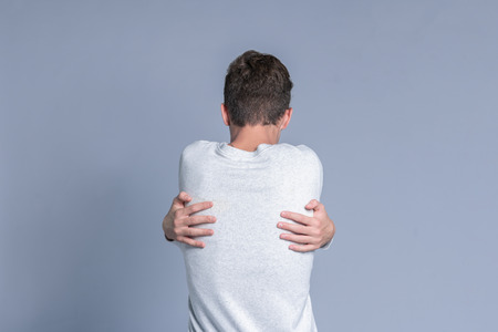 Teenager guy hugging himself over gray background