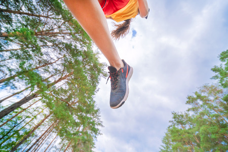 Closeup of athlete's feet running at the park. Fitness woman jogging outdoors. Exercising on forest...