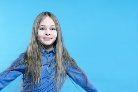 Portrait of a happy child girl over blue background. She is smiling and looking at the camera.の写真素材