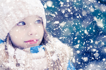 A girl child is looking at falling snowflakes  walking outdoors.の写真素材