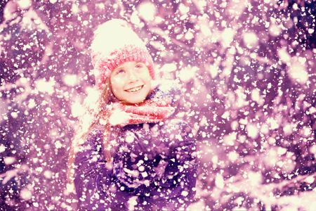 A happy girl child is looking up at snowfall in a winter forest.の写真素材