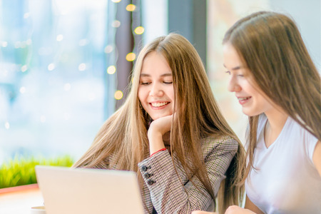 Teenage girls are watching film on laptop sitting in cafe.の写真素材