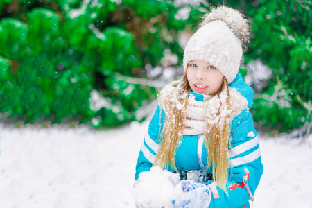 A beautiful blond child with a snowball in hand walking in a winter forest.の写真素材