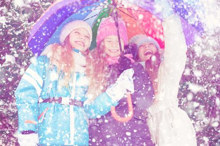 Happy little girls cheerfully laughing in snowy forest looking up and raising hand.の写真素材