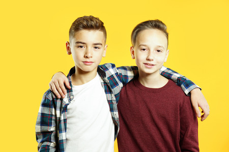 Child boys are best friends hugging and looking at the camera over yellow background. Two brothers togetherの写真素材