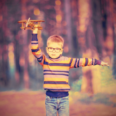 Funny little boy wearing glasses playing with toy airplane outdoors. Dreams of travelingの写真素材